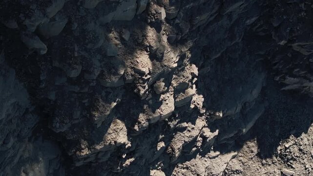 Exposed rock layers and loose rubble on the steep wall of an active quarry. The excavated slope reveals geological strata, fractured stone, and raw mineral deposits in an industrial extraction site.
