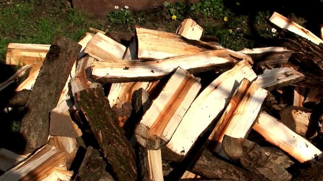 wood logs are chopped and dropped onto pile on the ground from top angle in slow motion ready for use in oven or fireplace in house during winter.