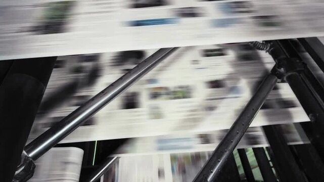Industrial offset press printing newspapers at high speed through metal rollers in factory setting with motion blur showcasing large scale mass production.