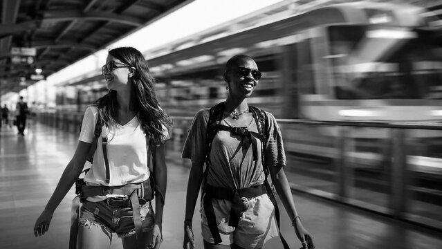 Two young women with backpacks walking along a platform as a train passes
