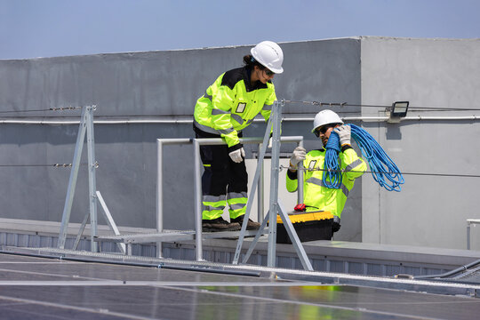 Workers installing solar panels on rooftop, Solar energy technicians preparing safety equipment for rooftop maintenance, Engineers handling safety ropes for solar photovoltaic installation