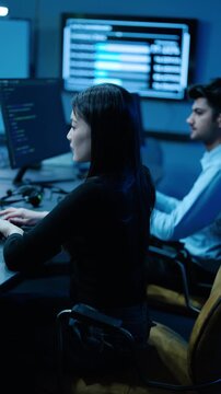 Professional IT experts work in a modern data center, managing software development, cybersecurity, and server network monitoring on multiple screens with complex code in a dark office environment.