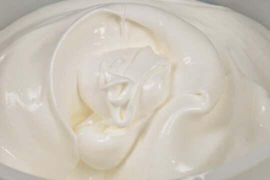 A close up view of fluffy whipped egg whites with sugar forming soft peaks inside a white mixing bowl