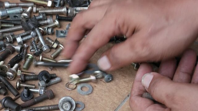 Close Up of Hands Sorting Mixed Screws and Bolts on Floor