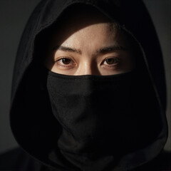 Naklejka premium Mysterious woman in black hoodie and face mask looking at camera with dramatic cinematic lighting, close up portrait
