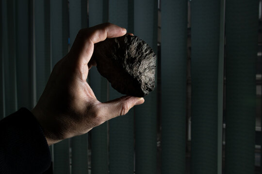 Holding a natural phosphorite round-shaped rock stone in hand at a laboratory, blurred vertical blinds in the background
