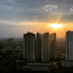 Obraz premium Sun rays breaking through clouds above a high rise city skyline, creating a dramatic urban landscape. A combination of powerful natural light, architecture, and modern city atmosphere.