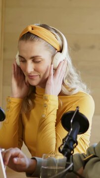 Vertical video: Putting headset, host in yellow top adjusting in studio to record, with mics