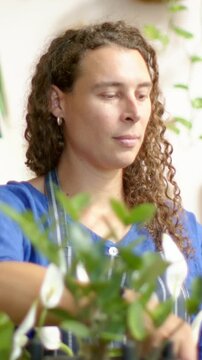 Vertical video: Reaching forward, nonbinary person adjusting leaves for care in studio, with apron