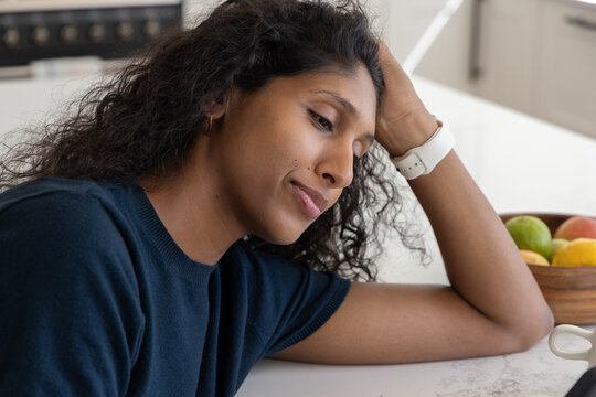 Adult woman leaning on countertop in kitchen, wearing navy top, wristwatch near fruit bowl