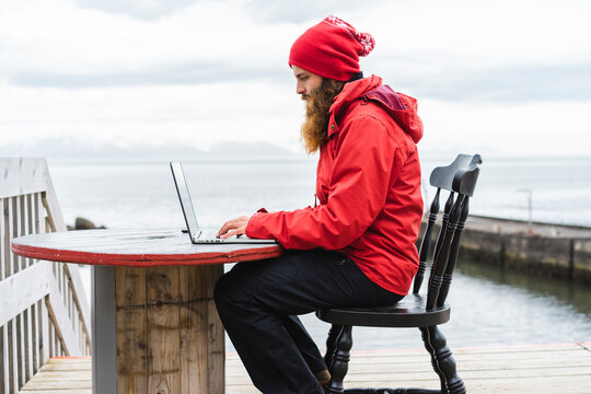 Iceland, North of Iceland, man sitting in front of the sea using laptop