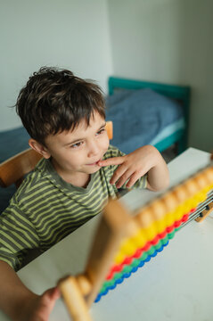 Inquisitive child studying mathematics with colorful abacus indoors