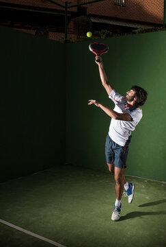 Male athlete servicing ball while playing padel tennis in sports court at night