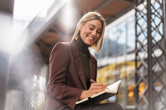 Smiling young businesswoman taking notes in the city
