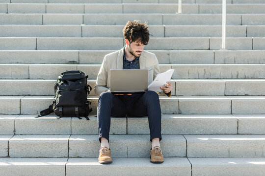 Pensive man with laptop sitting on steps checking documents