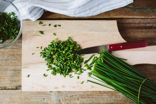 Chopped and whole chives and kitchen knife on wooden board