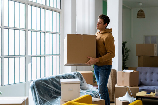 Young man carrying box while moving into new home