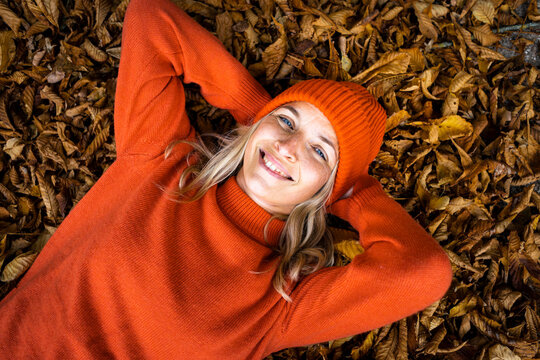 Smiling mature woman lying with hands behind head on autumn leaves