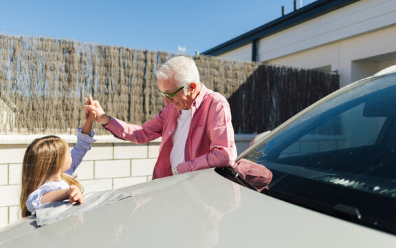 Playful grandfather and granddaughter boxing by a car in the backyard