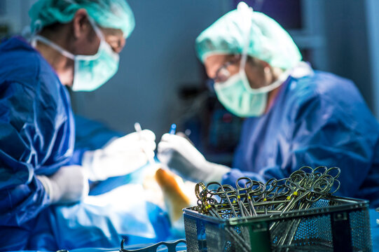 Male surgeons performing operation by scissors in emergency room at hospital