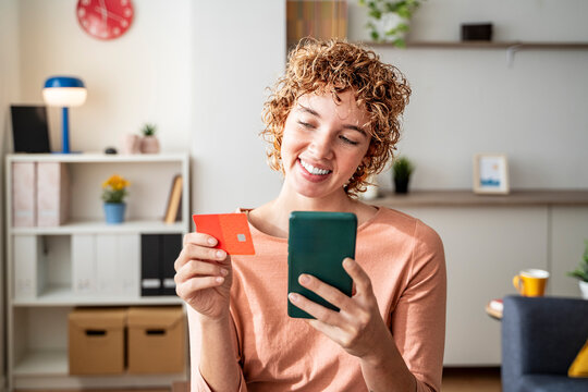 Smiling woman shopping online with smartphone and credit card at home