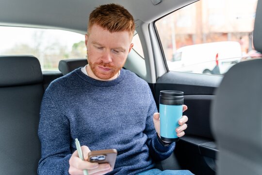 Businessman using smartphone and holding coffee in backseat