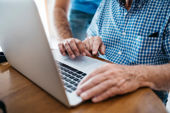 Adult grandson teaching his grandfather to use laptop, close-up