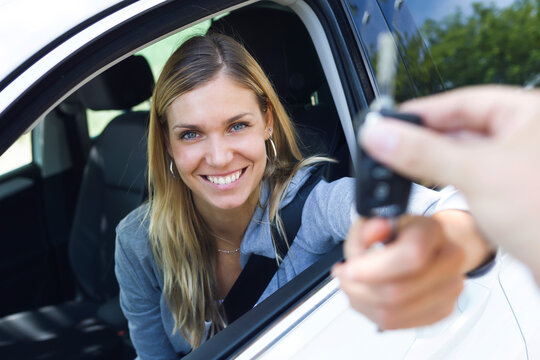 Portrait of smiling young woman looking at camera while holding car keys and give it to someone through the window