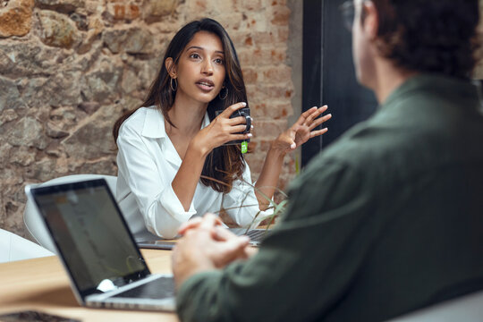 Businesswoman holding coffee mug discussing with businessman at desk in office