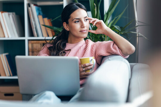 Student relaxing on cozy sofa with laptop doing homework