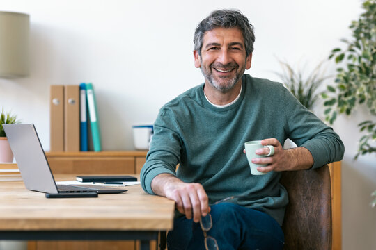 Smiling adult relaxes with coffee at office desk