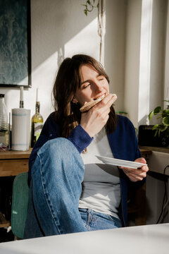 Smiling woman eating bread for breakfast at home in sunlight