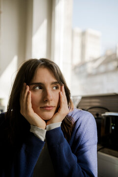 Thoughtful young woman looking out window at home