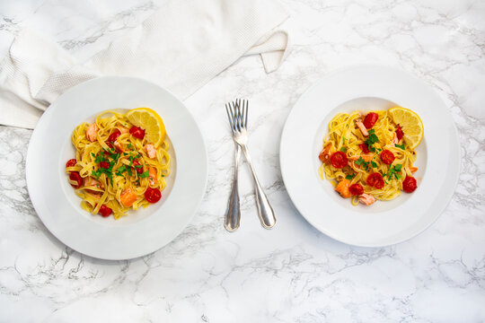 Two plates of salmon tagliatelle with tomatoes on marble