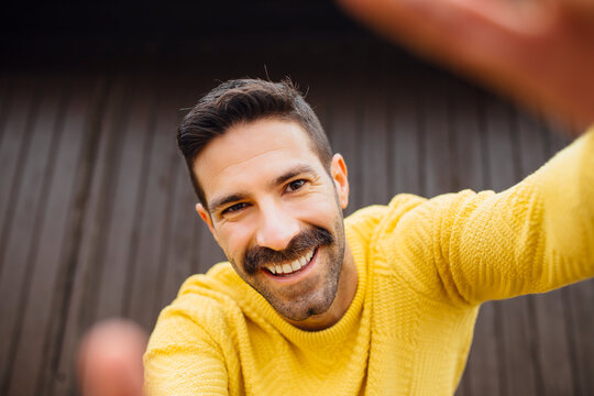 Smiling man with mustache in yellow sweater taking selfie