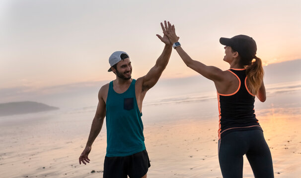 Athletes couple hitting five on the beach at sunset