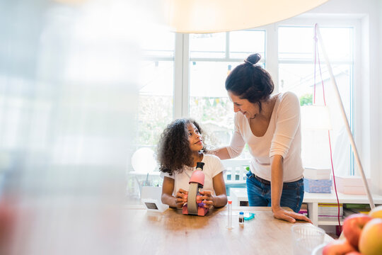 Mother helping daughter with homework, using microscope