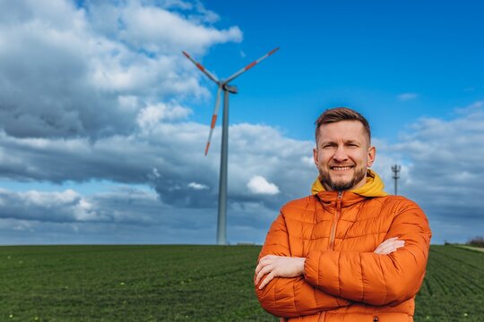 Smiling engineer with arms crossed by a wind turbine