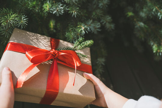 Hand of girl holding Christmas gift box tied with red ribbon