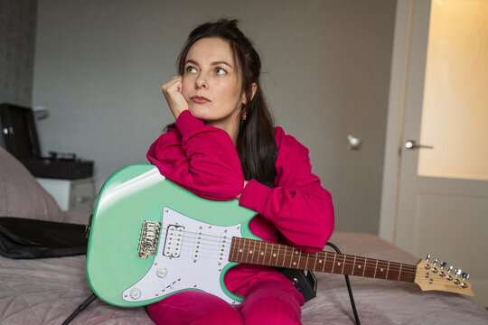 Woman sitting on a bed holding an electric guitar and thinking
