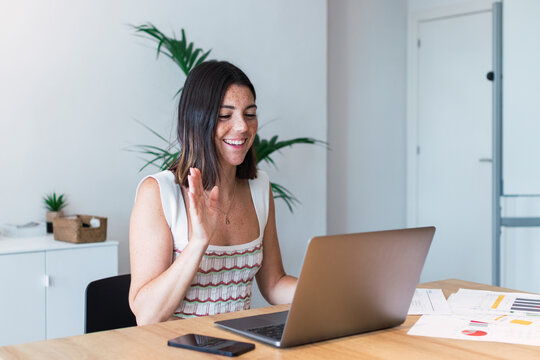 Smiling young businesswoman on video call waving at laptop