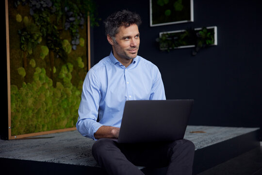 Smiling businessman with laptop sitting in office