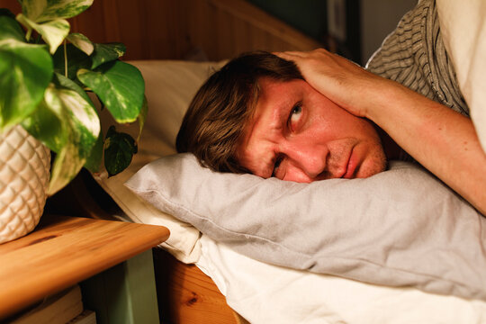Man covering ears lying down on bed at home