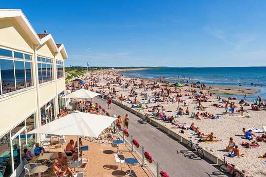 Crowded summer beach by the sea with people relaxing and sunbathing by a boardwalk