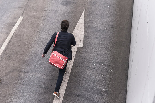 Rear view of businessman running on road with arrow sign