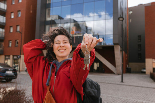Smiling homeowner showing house key outdoors in modern city