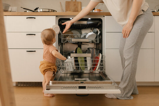 Mother and toddler loading the dishwasher in the kitchen