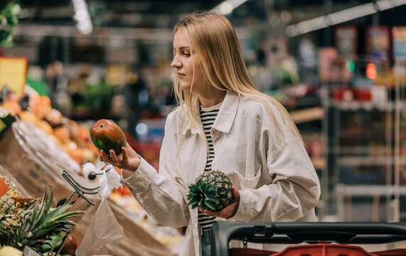 Woman with blond hair examining fruits in supermarket