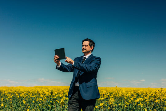 Businessman using tablet in yellow rapeseed field under blue sky