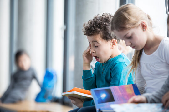Exhausted student struggles to focus on his studies while surrounded by the distractions of the classroom